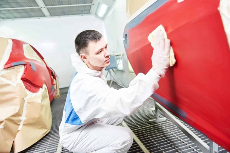male paint finisher in overalls working on a red car door in automotive workshop