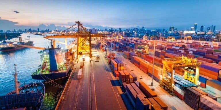 Containers, ships, trucks and crains in a busy Asian container port at dusk