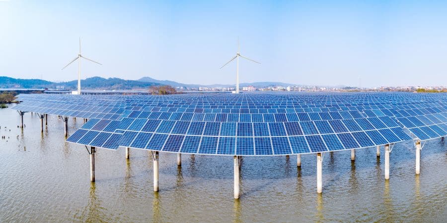 Large solar panel array with wind turbines in the background