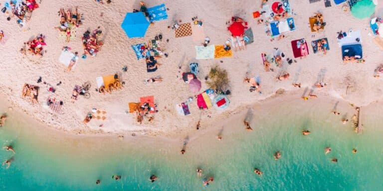 Tourists swimming and sunbathing on a sunny beach with clear blue water