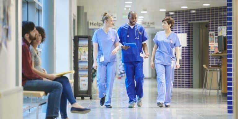 Two nurses and a doctor talking as they walk along a hospital corridor