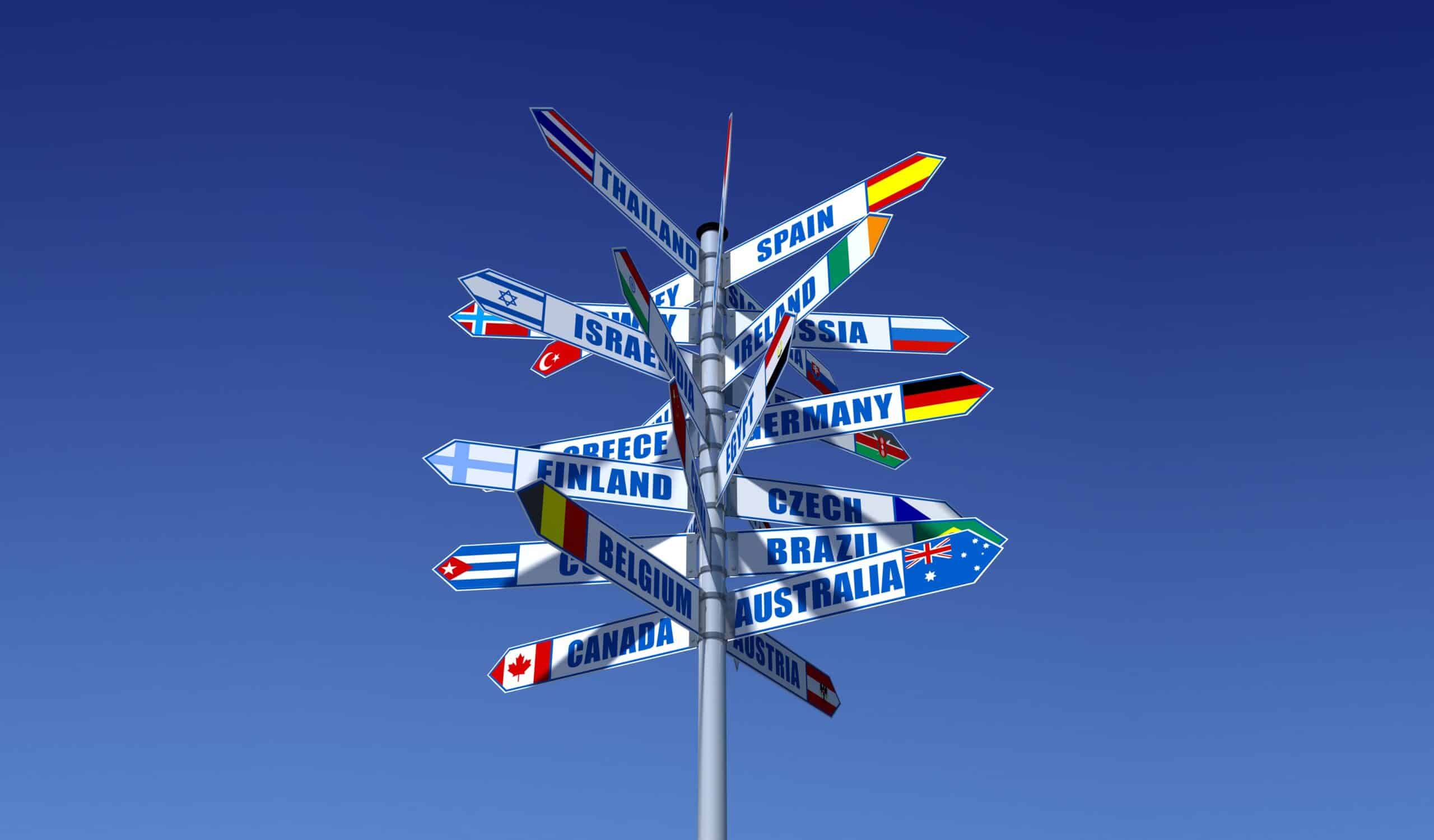 Signpost pointing to many different countries shown against clear blue sky