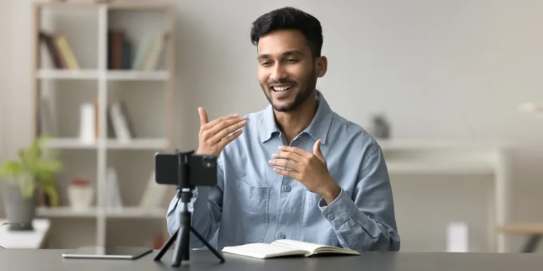 Smiling young Indian man using a smartphone on a tripod to complete a video survey at home