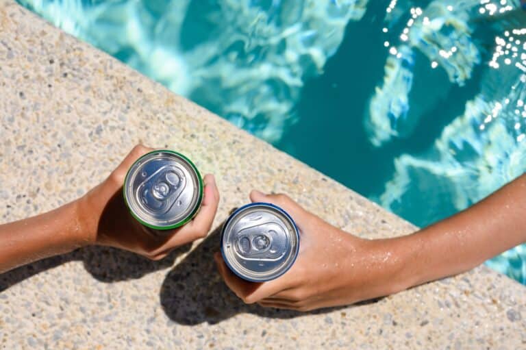 two friends at los angeles pool drinking sweetened soda canned drinks together in the sun