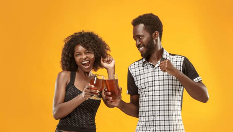 young jamaican and nigerian londoners drinking malted drinks together at a party yellow background