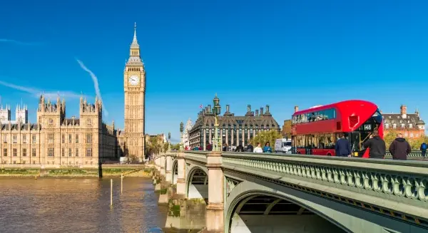 Houses of Parliament, London, on a sunny day. A red bus crosses Westminster Bridge in the foreground
