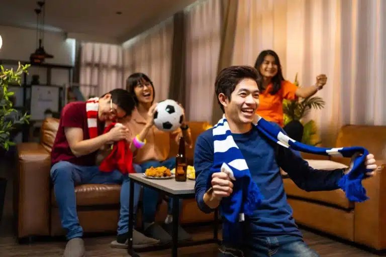 Four Asian football fans watching soccer match on TV at home