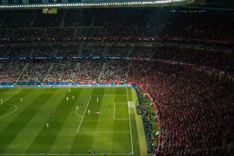 Soccer fans watching match at night in floodlit stadium. The stands are full and the players can be seen on the pitch