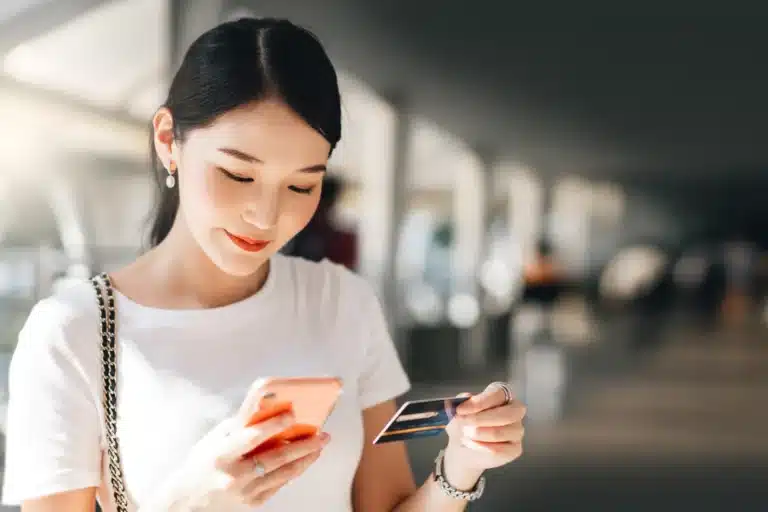 Young Asian woman entering her credit card details on her phone to purchase insurance