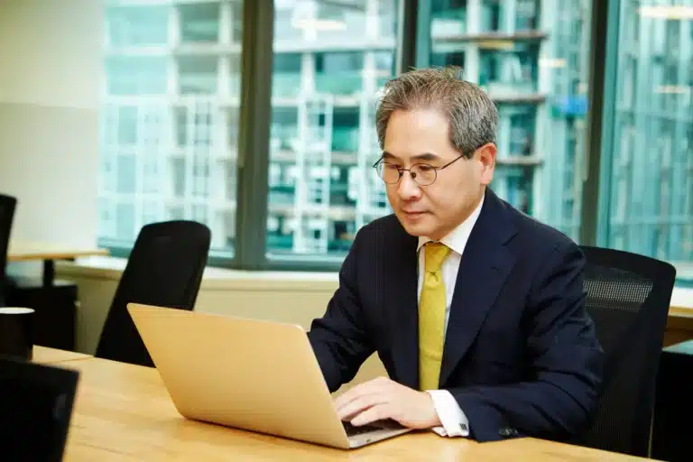 Senior Korean policy expert taking part in online interview via his laptop in the office