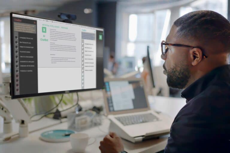 Qualitative moderator sitting in front of his laptop and external monitor reviewing interviews conducted by AI chatbot